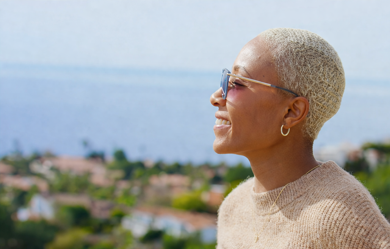Woman with short blonde hair wearing sunglasses and a beige sweater outdoors.
